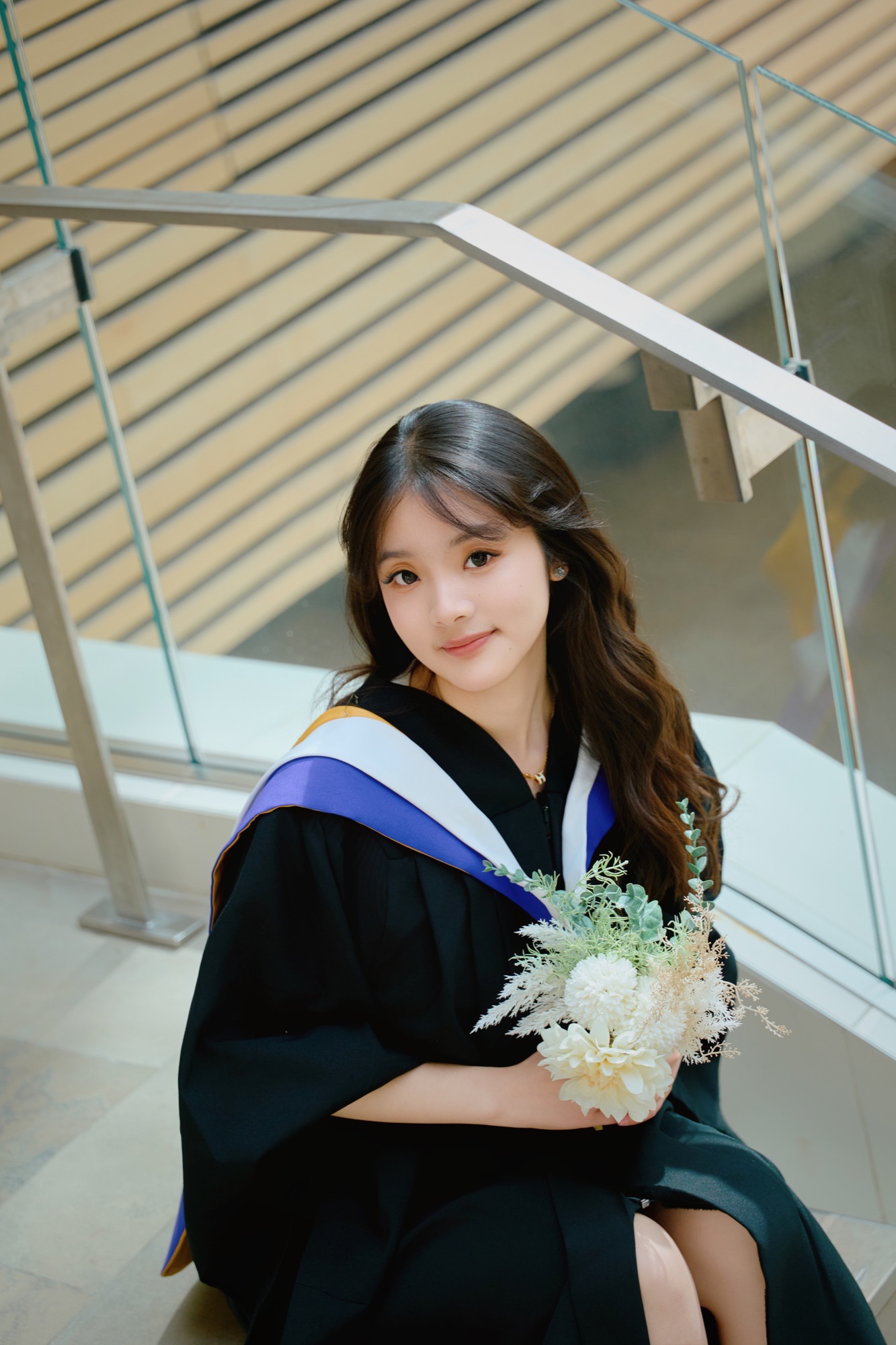 A graduate seated beside a staircase