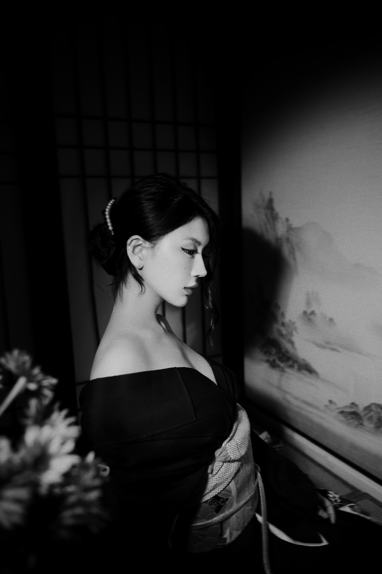 A black and white side-profile portrait beside a painted folding screen