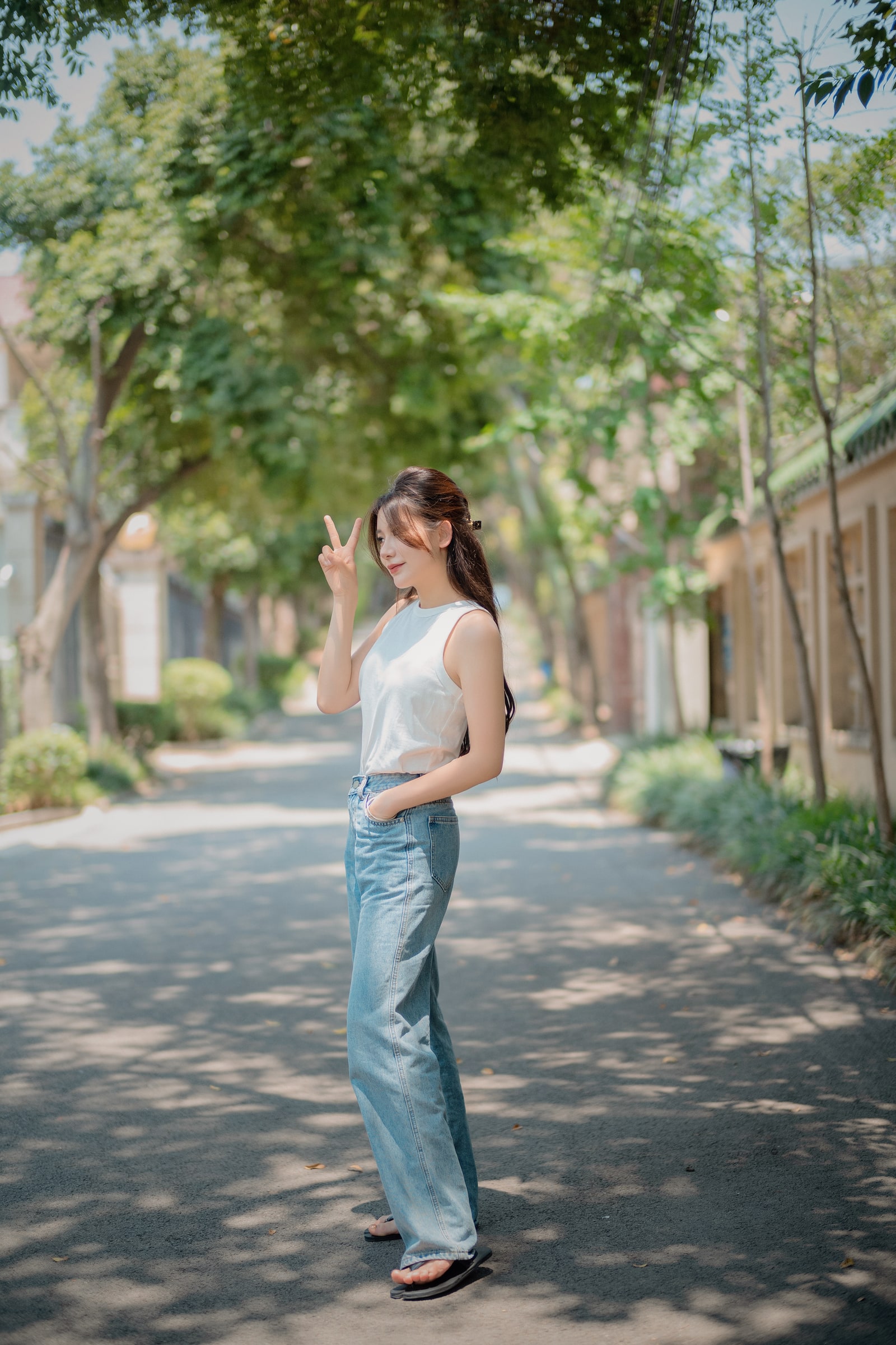 A portrait in a white top and blue jeans on a tree-lined street