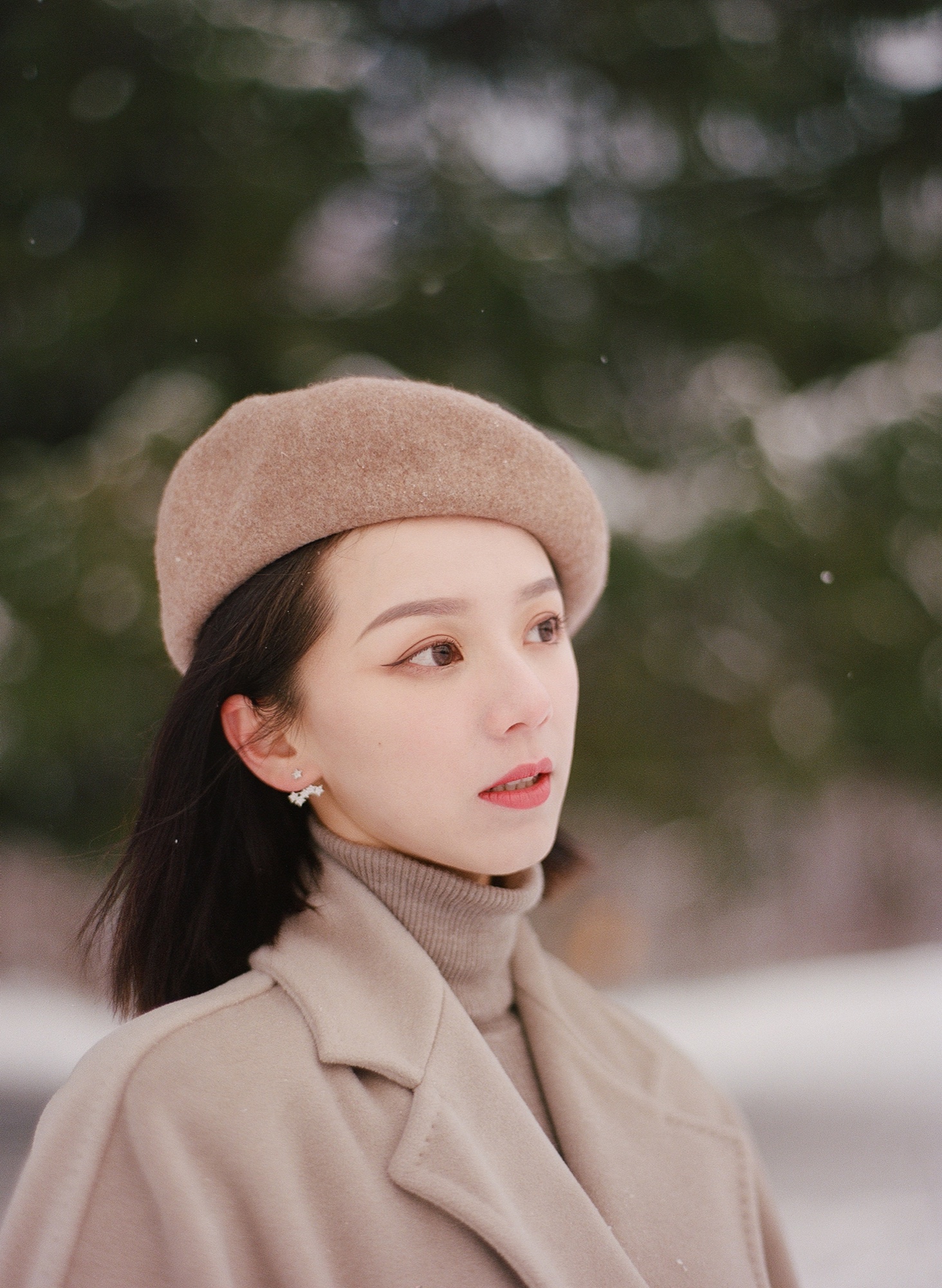 A close portrait in a beige beret and coat against winter trees