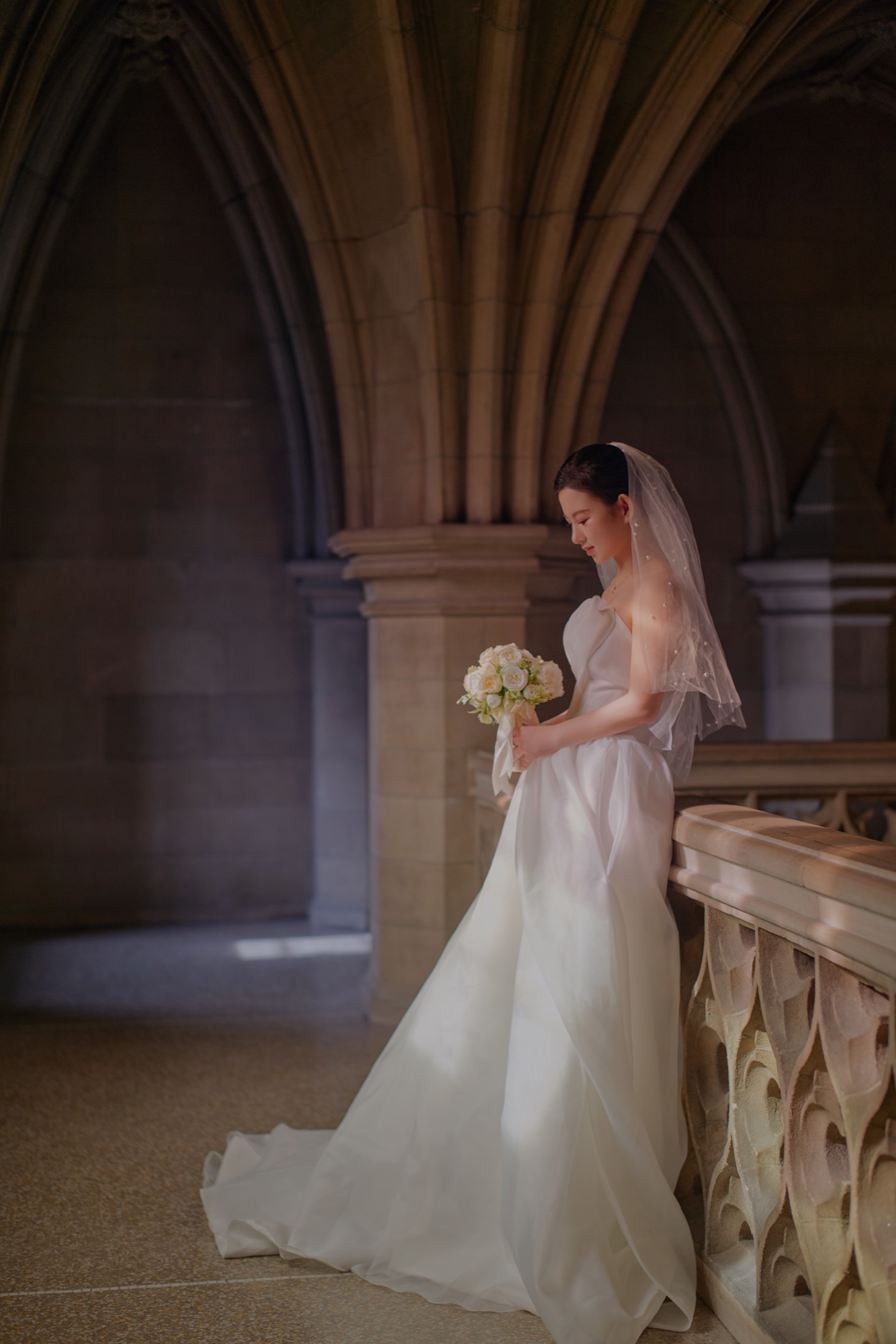 A bride holding a bouquet beside a carved stone balustrade