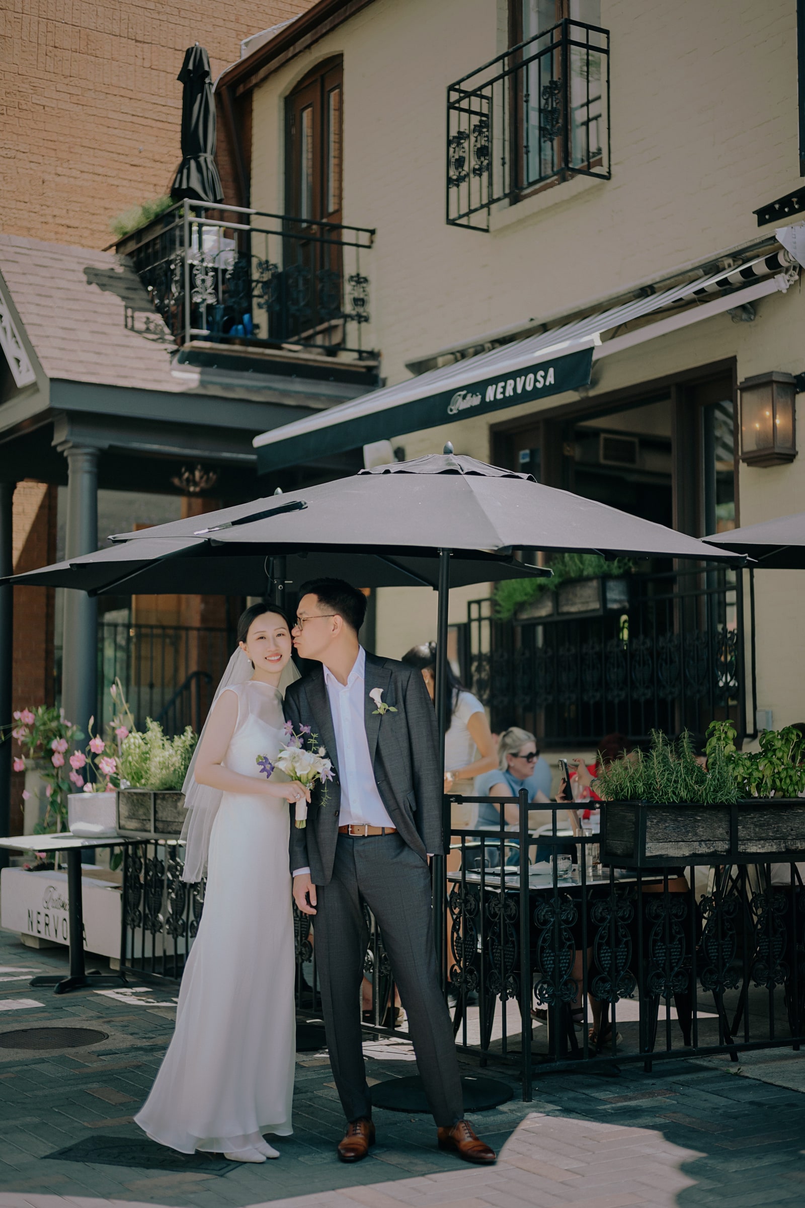 A wedding couple sharing a kiss beneath a cafe terrace umbrella